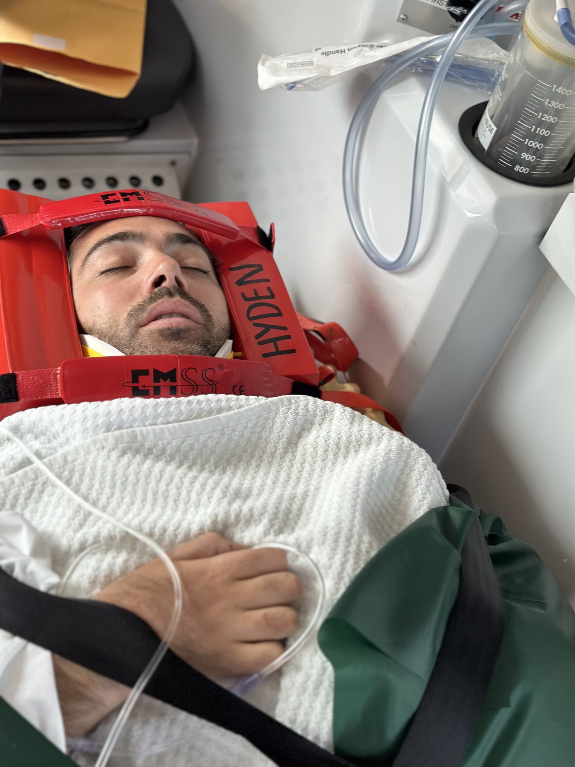 Man in red frame around head with white blanket and tube on way to hospital